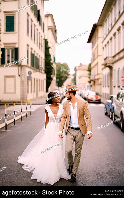 Wedding in Florence, Italy. Interracial wedding couple. African-American bride and Caucasian groom walk along the road among cars