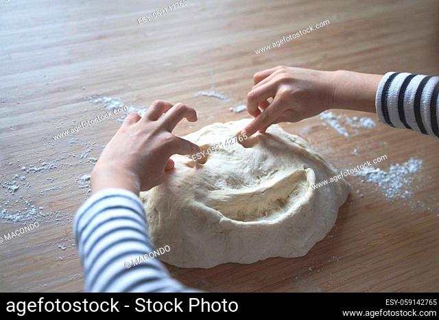 top view close up portrait of Caucasian little girl with stripped shirt drawing a smiling face in the dough at home on a kitchen wood cutting board in natural...