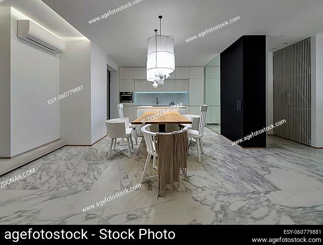 Kitchen in a modern style with white walls and gray tiles with patterns on the floor. There is a wooden table with white chairs, kitchen island with stove
