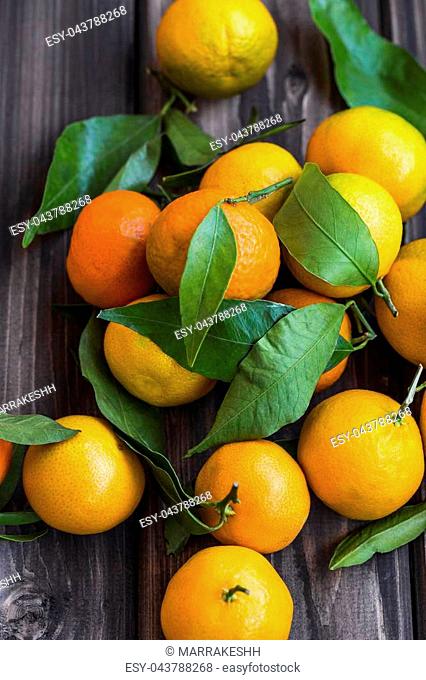 Fresh clementines heap with leaves on wooden background, top view of sweet organic tangerine or clementines citrus fruits
