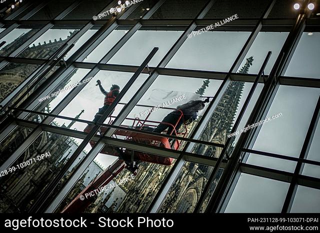 28 November 2023, North Rhine-Westphalia, Cologne: The glass façade of Cologne Central Station is cleaned by window cleaners in front of Cologne Cathedral