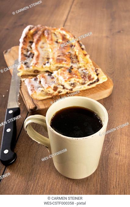 Cup of black coffee, knife and Danish pastry with marzipan on wooden board and table