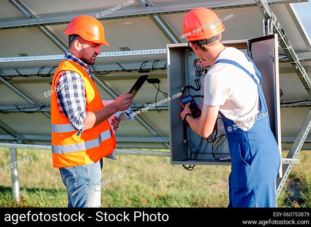 Worker and foreman cheking wires of solar panels. Maintaining works on solar energy station