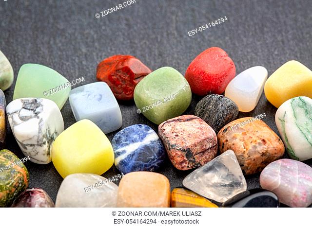 polished, semiprecious, colorful gemstones against gray slate stone with a copy space