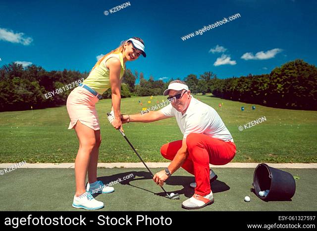 Golf pro teaching a woman student of the driving range practicing with her