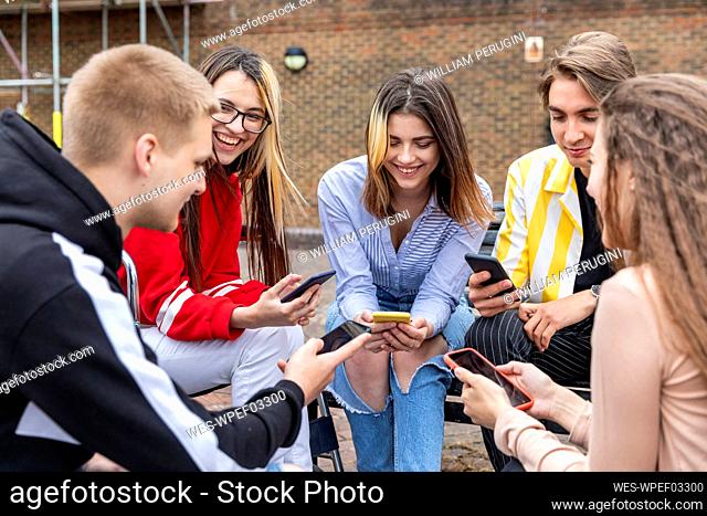 Cheerful male and female friends using smart phones while spending leisure time in city