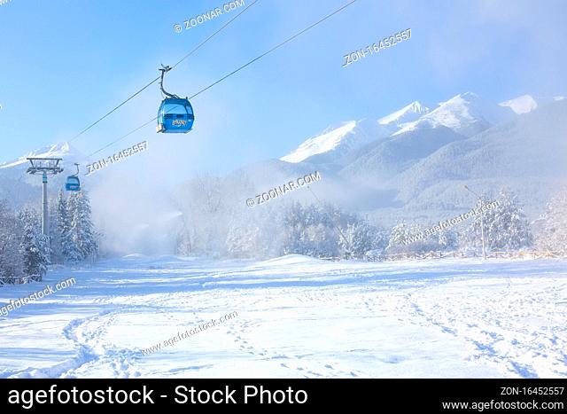 Bansko, Bulgaria - December 5, 2019: Winter ski resort panorama with blue gondola lift cabins, forest pine trees, Pirin mountain peaks view and slope