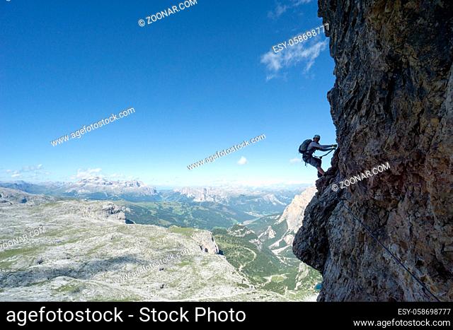 Horizontal view of an attractive female climber on a steep Via Ferrata in the Italian Dolomites with a great view behind