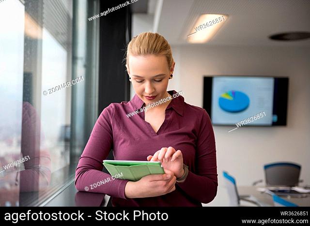 Blonde businesswoman in casual clothes working on tablet computer at modern startup business office interior. Young people group on team meeting blured in...