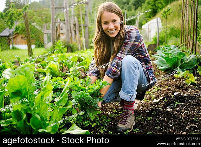 Happy young woman planting vegetables in garden