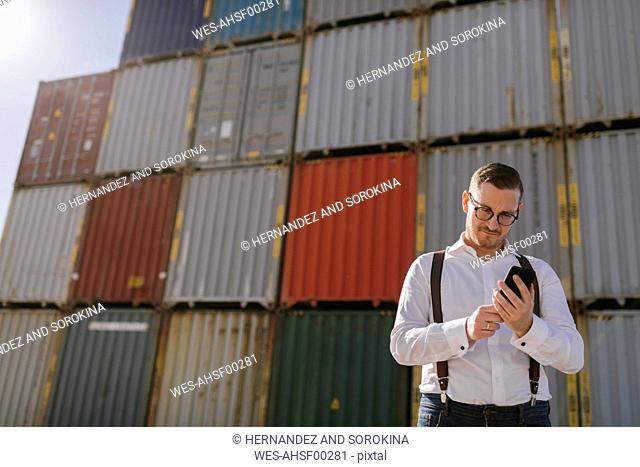 Manager in front of cargo containers on industrial site using cell phone