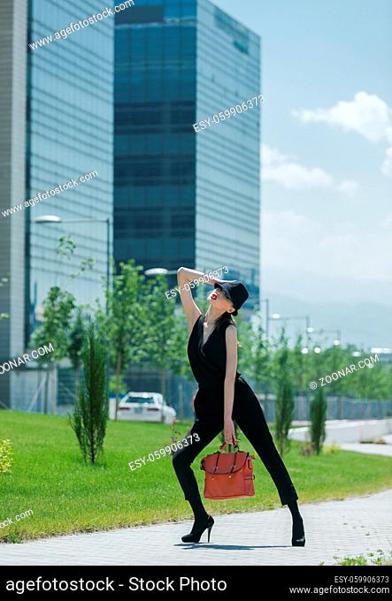 Stylish asian girl in a black suit and hat, posing with a glass wall