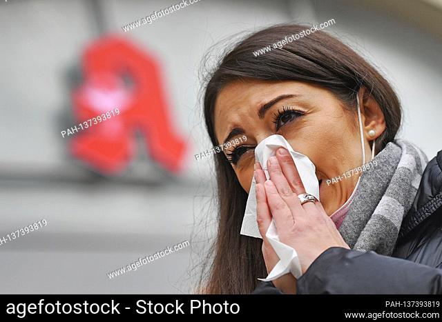 Topic picture Coronavirus pandemic in autumn / winter-young woman with a mouthguard hung on her ear, mask wipes her nose with a paper handkerchief, sniffing