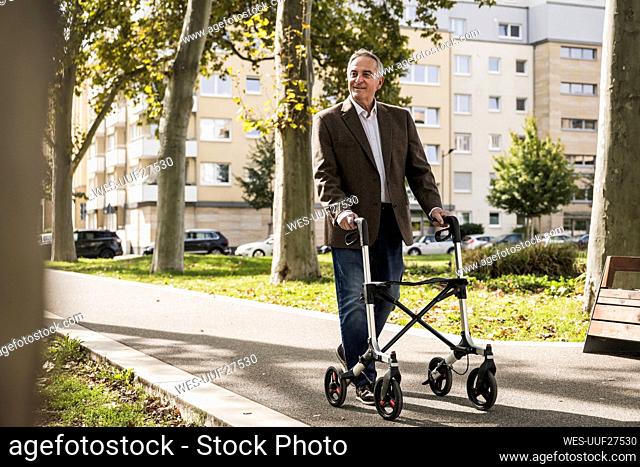 Smiling senior man walking with mobility walker on footpath