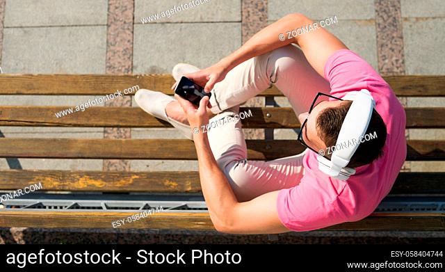 Top view of smiling man sitting outside with mobile phone and headphones