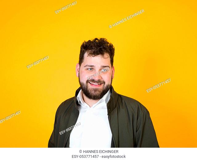 cool man with black beard and black hair is posing in front of orange background in the studio