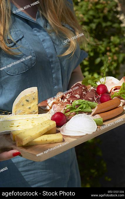 charcuterie board with ham, sausage, cheese, and radishes