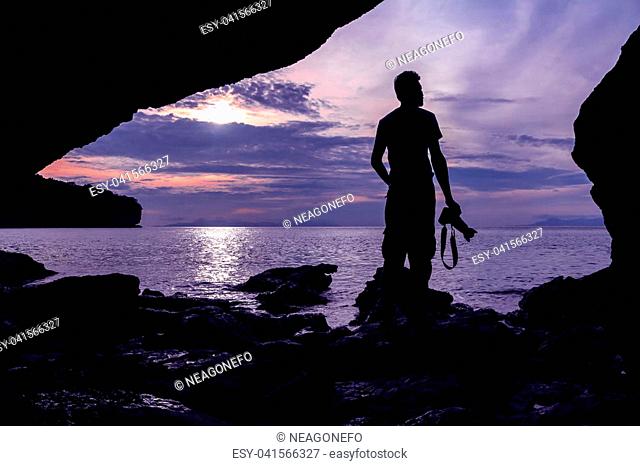 Silhouette photographer in front of the cave near the sea with purple sky in the morning