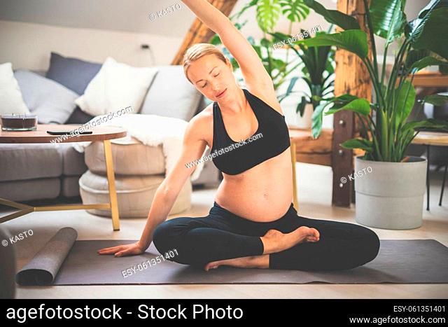 Young beautiful pregnant woman training yoga at home in her living room. Motherhood, pregnancy, healthy lifestyle and yoga concept