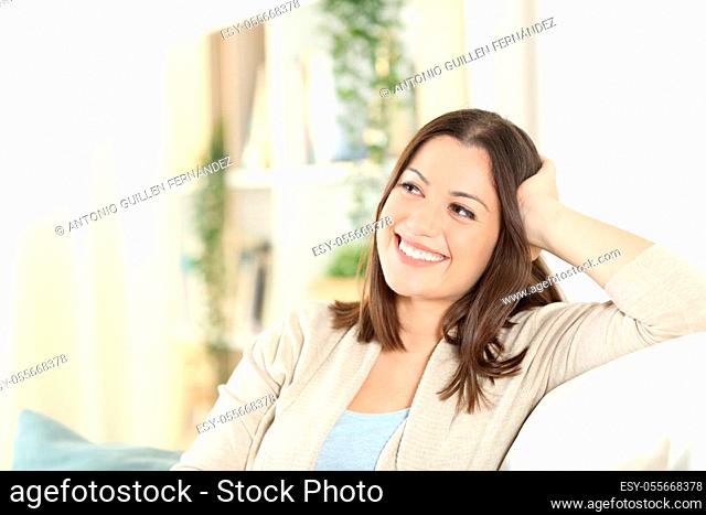 Happy woman thinking looking at side sitting on a couch in the living room at home