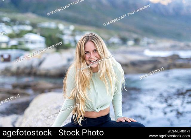Happy young woman with blond hair sitting on rock