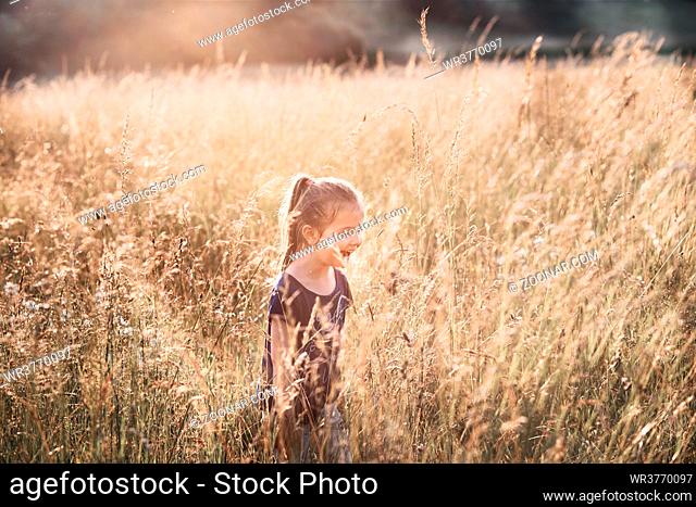 Little happy smiling girl walking through a tall grass in the countryside. Candid people, real moments, authentic situations