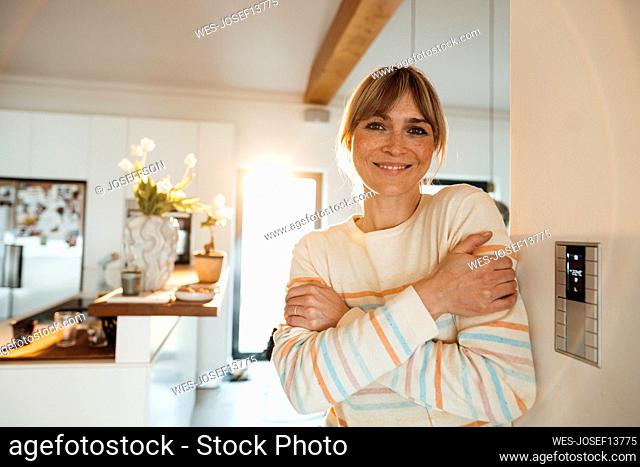 Happy woman hugging self near thermostat on wall at home