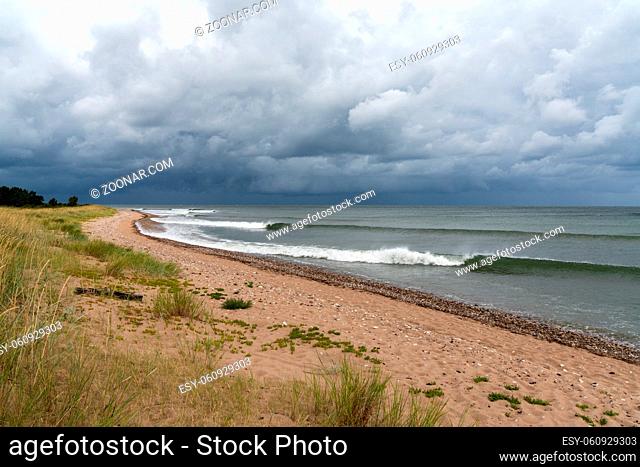 Sets of neat waves breaking on a sandy beach with marsh grass and sand dunes and a dark ominous sky overhead