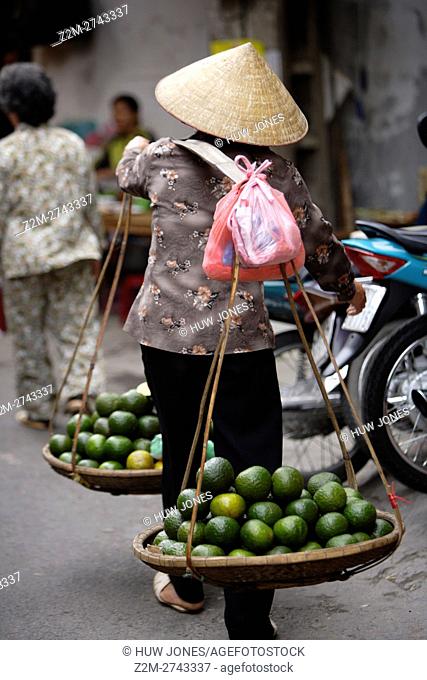 Woman carrying a traditional Vietnamese ‘don ganh’ yoke, Old Quarter, Hanoi, Vietnam