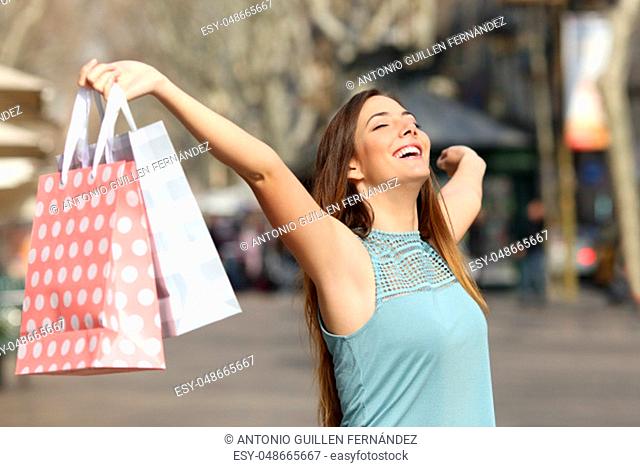 Happy shopper holding shopping bags raising arms in a street