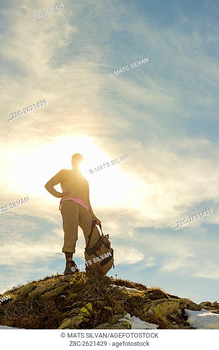 Woman with her backpack standing on a mountain top and sunshine in Grisons, Switzerland