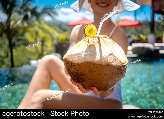 Woman in her tropical vacation having a coconut snack showing it into the camera