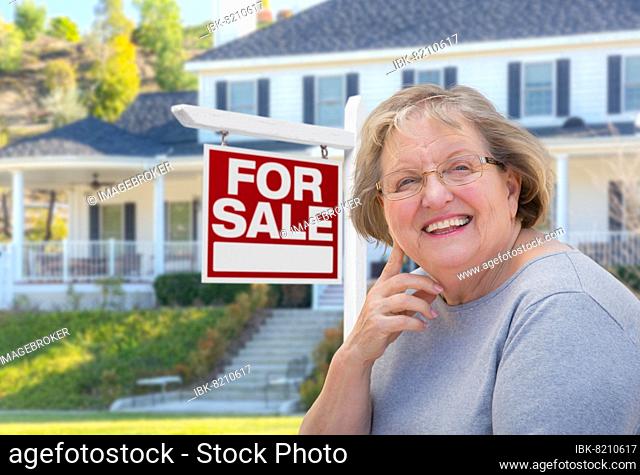 Senior adult woman in front of home for sale real estate sign and beautiful house
