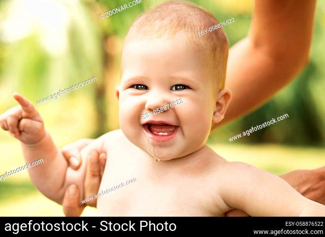 Portrait of a beautiful baby holding the mother's hand against green nature background outdoors