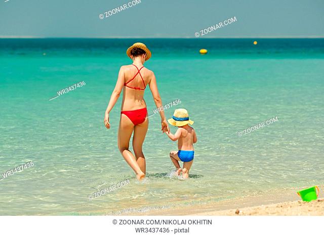 Two year old toddler boy walking on beach with mother