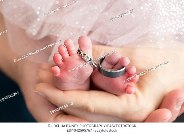 Mom and dad hands holding a newborn baby with wedding rings on the feet of the child