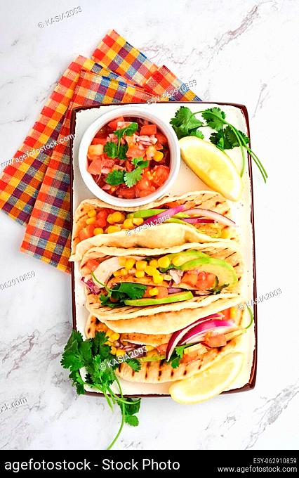 Mexican tacos with grilled chicken, avocado, corn kernels, tomato, onion, cilantro and salsa at white stone table. Traditional Mexican and Latin american street...