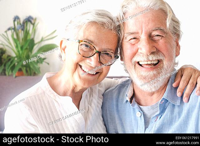 Portrait of cheerful senior couple embracing and laughing. Elderly happy couple relaxing in front of camera sitting in living room