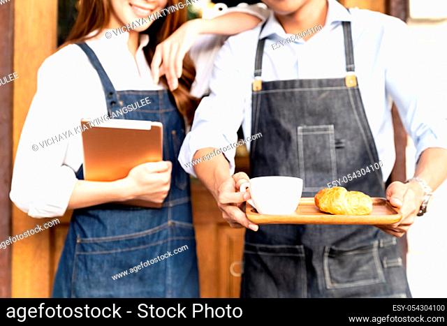 Closeup Asian young adult owners of Small business cafe holding coffee set and digital tablet in front of coffee retail shop