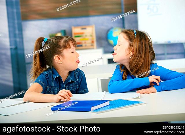 Children sticking out tongue to each other in primary school classroom. Elementary age children