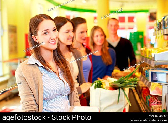 Lächelnde Frau steht in einer Warteschlange an der Kasse im Supermarkt