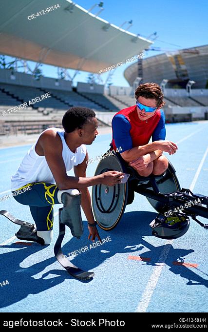 Male amputee and wheelchair athletes talking on sunny sports track