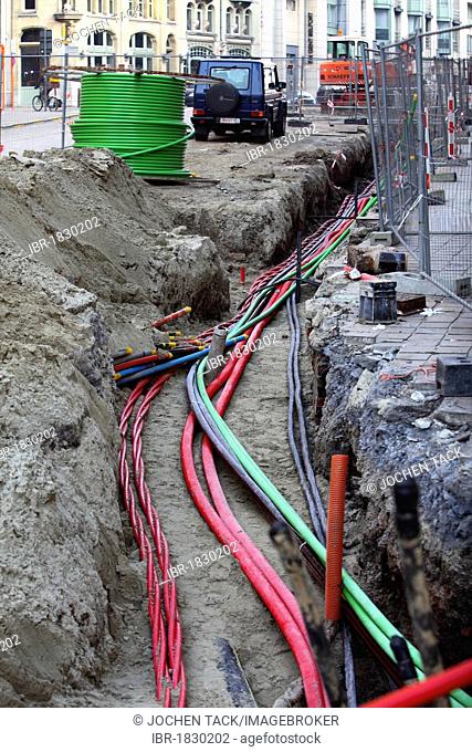 Installation of various cables in a building site, power lines and telecommunication cables, some in protective tubes, placed in the ground