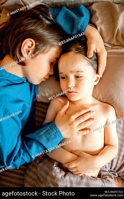 Boy taking care of sick brother lying on bed at home