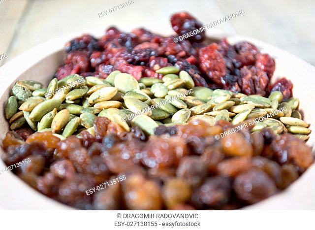 Bowl full with dry fruits and pumpkin seeds on the wooden table, shoot with selective focus
