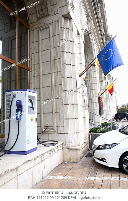 01 December 2019, Romania, Bukarest: An electric vehicle parks next to a charging station in front of a building of the Ministry of the Environment and Climate...
