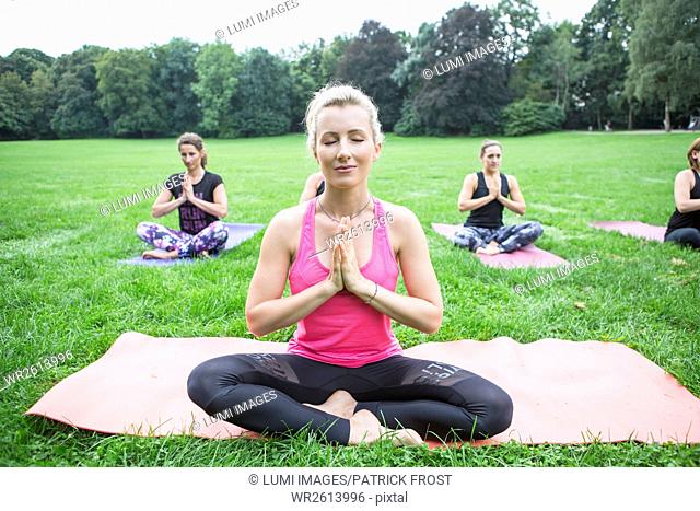 Young women practicing yoga in park hands folded