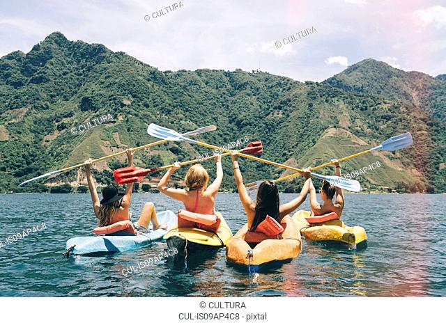 Rear view of four female friends celebrating in kayaks on Lake Atitlan, Guatemala