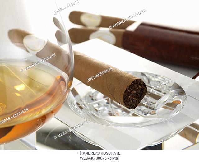 Cigar in ashtray with glass of cognac, close-up