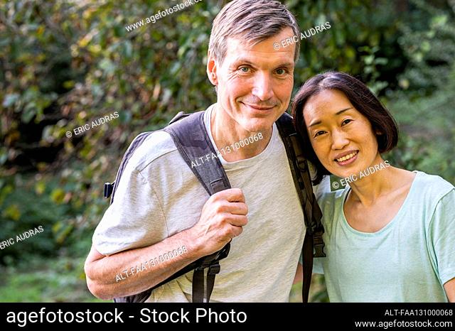 Middle-aged diverse couple looking at camera while hiking out in the woods